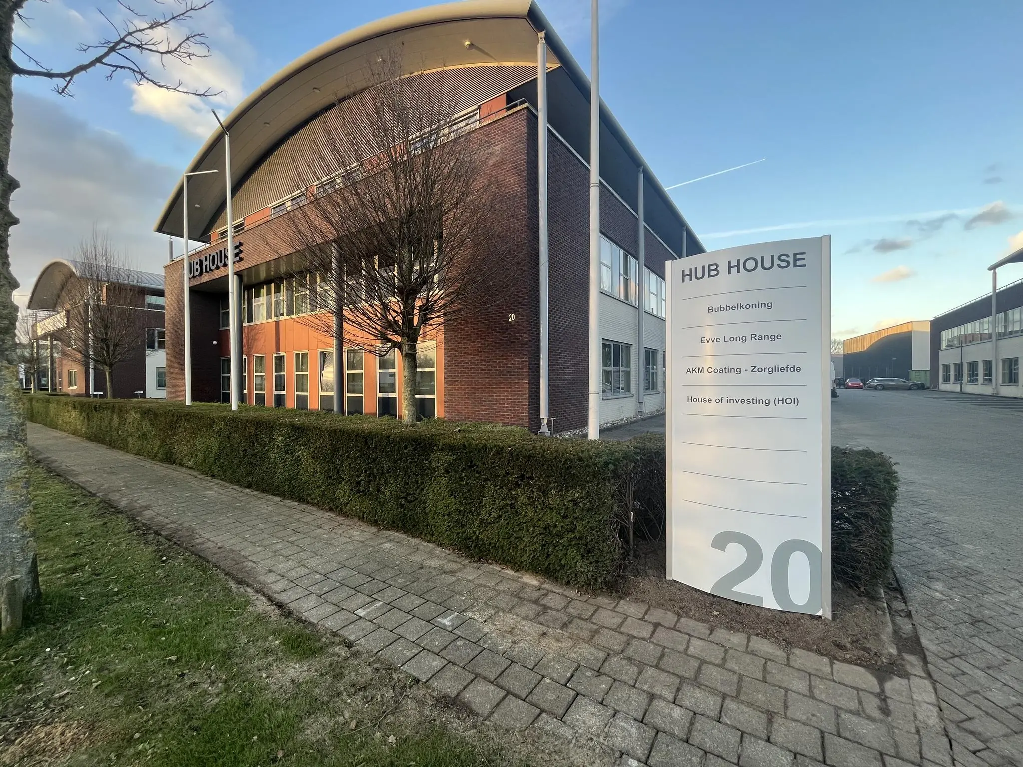 Kantoorgebouw HUB HOUSE met bedrijfsnamen op een wit bord en huisnummer 20 aan een betegeld pad.